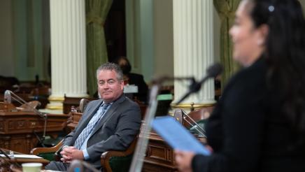 Assemblymember O'Donnell listens to Assemblymember Carillo speaking on the Assembly floor during a ceremony honoring him and other retiring Assemblymembers